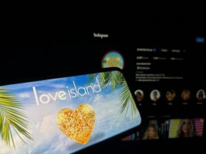 Cell phone screen with Love Island show logo showing on it being held in front of computer screen with Instagram pulled up