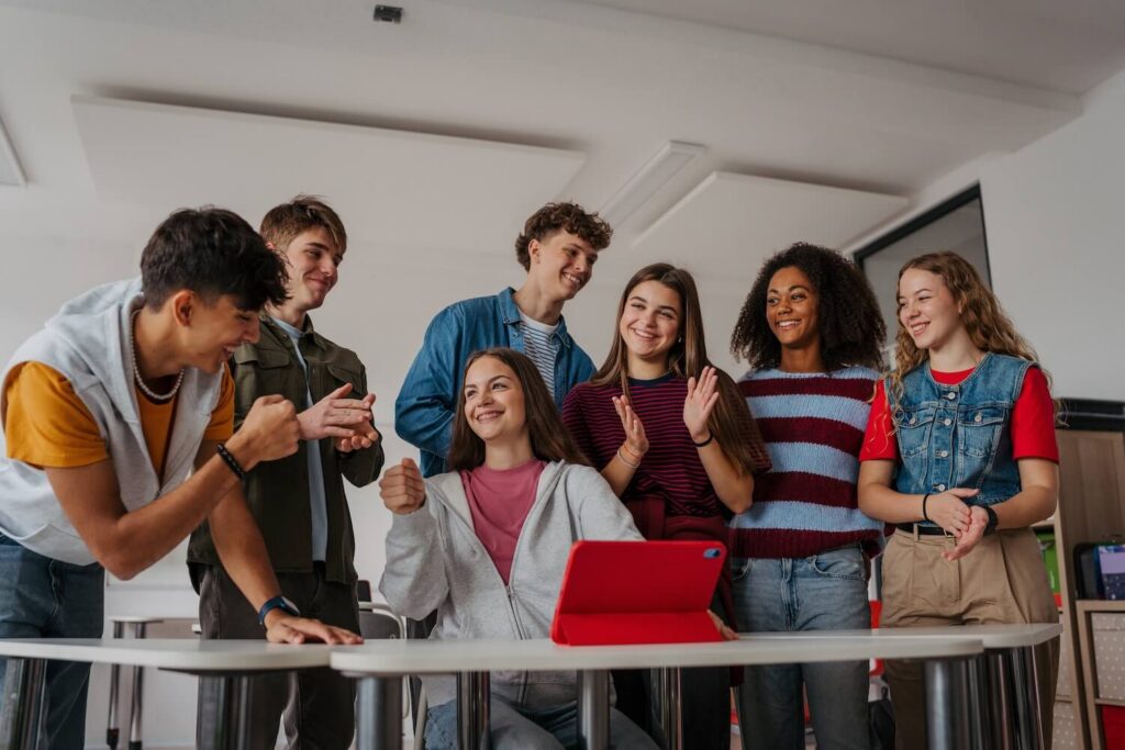 Group of teen girls and boys in classroom smiling and working together