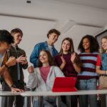Group of teen girls and boys in classroom smiling and working together
