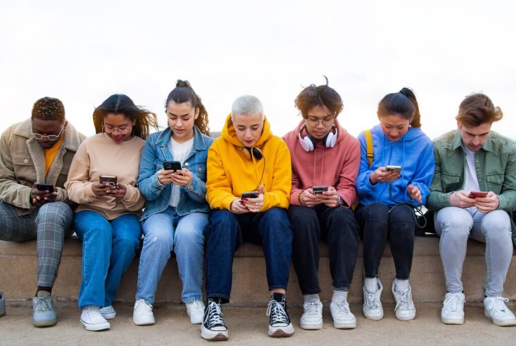 Group of teens sitting in a row all looking at their phones