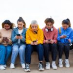 Group of teens sitting in a row all looking at their phones