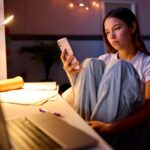Teen girl sitting at her desk in her bedroom looking at social media on her phone