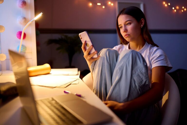 Teen girl sitting at her desk in her bedroom looking at social media on her phone