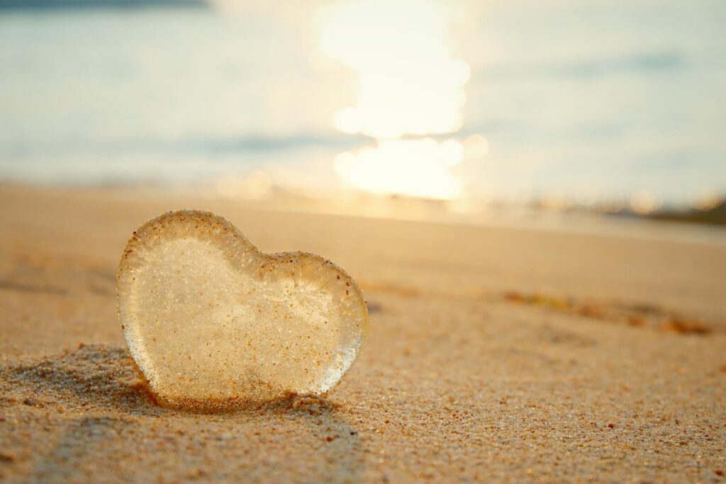 Glass heart in sand on beach with sunshine in background