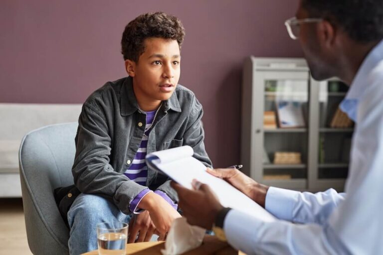 Teen boy sitting across from male therapist during therapy session