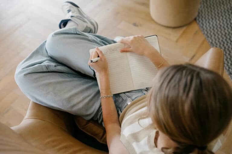Teen girl sitting in comfortable chair while writing in her journal to cope with her emotions