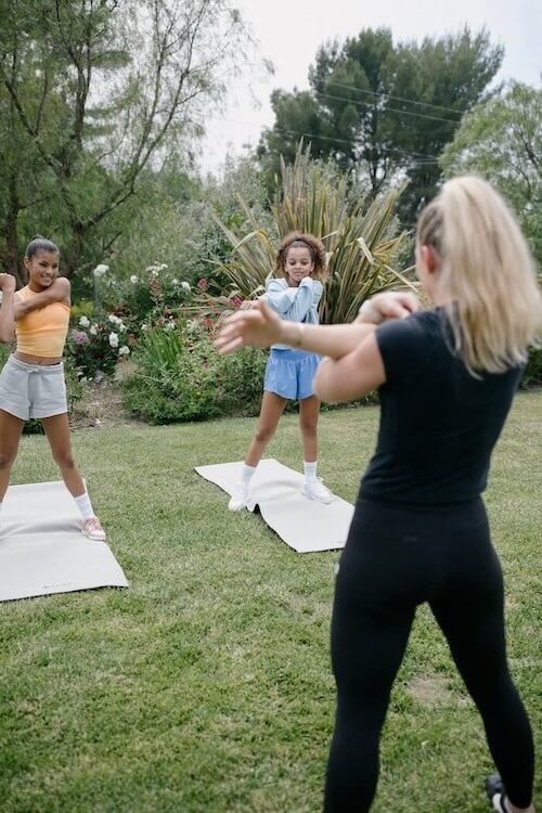 Teen girls stretching with exercise coach outside on exercise mats in the grass